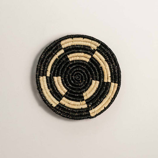 Round woven black cream seagrass wall basket with concentric stepped ring block pattern on white background product image.