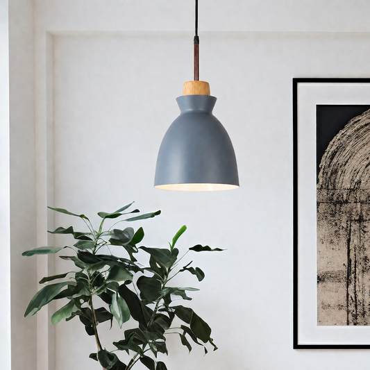 A modern pendant light with a matte slate blue-gray dome shade, a natural wood finial, and a dark brown cord, hanging in a minimalist room next to a green plant and framed wall art.