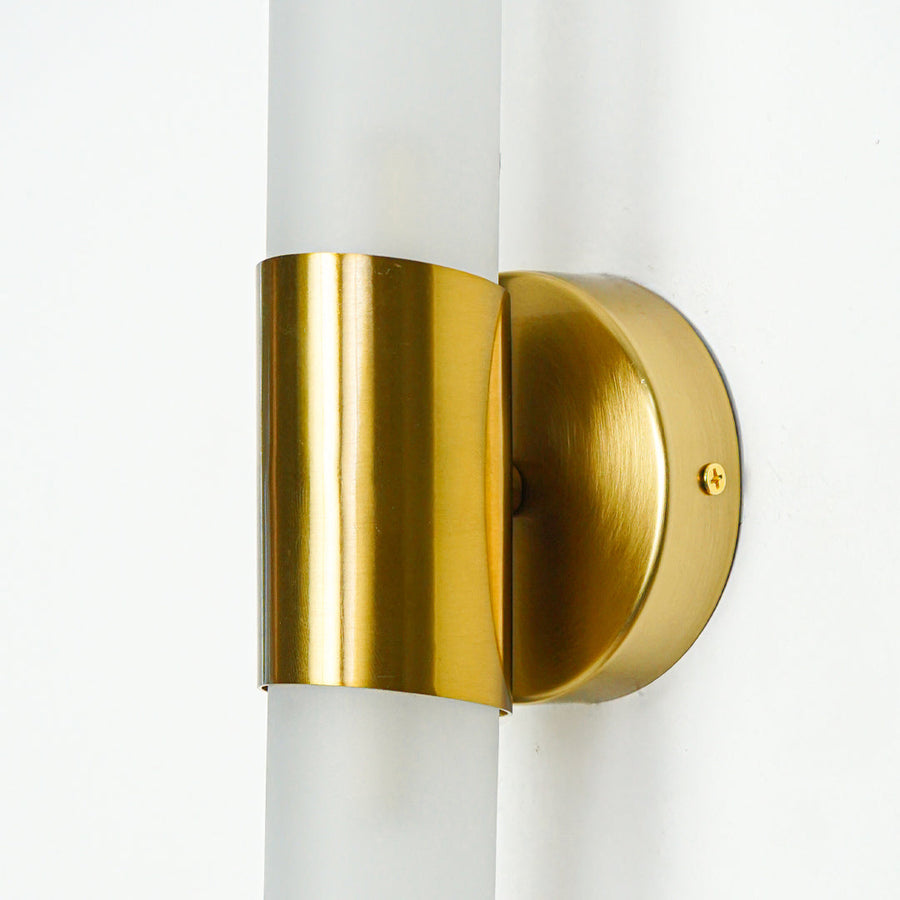 Close view of gold metal wall light with frosted glass tube highlighting premium modern lighting design on neutral background.