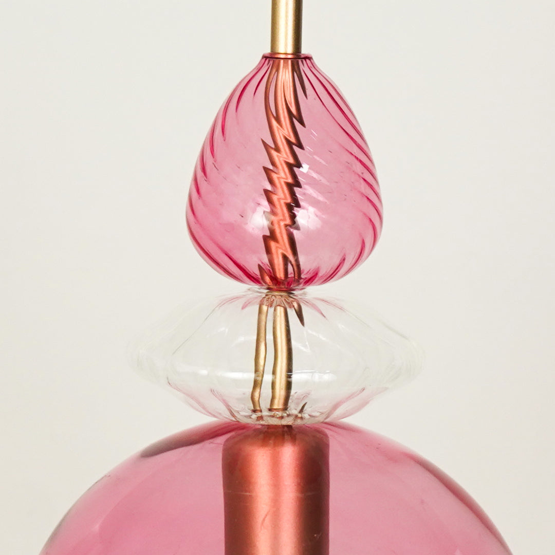 Closeup of pink glass pendant light with rose gold metal fitting for elegant dining room and modern interior lighting.