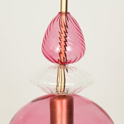 Closeup of pink glass pendant light with rose gold metal fitting for elegant dining room and modern interior lighting.