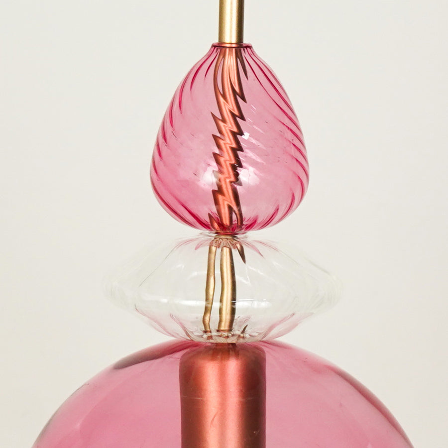 Closeup of pink glass pendant light with rose gold metal fitting for elegant dining room and modern interior lighting.