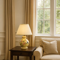 Elegant floral ceramic table lamp with gold base and white pleated shade brings a timeless and charming accent to any living space.