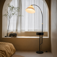 Modern black arc floor lamp with pleated fabric shade beside bed adding warm ambient lighting for cozy bedroom interiors.