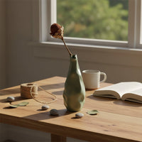 A sculpted green vase displayed in a minimal lifestyle setting highlighting its organic flowing shape and artistic form that brings a modern decorative appeal to any space.