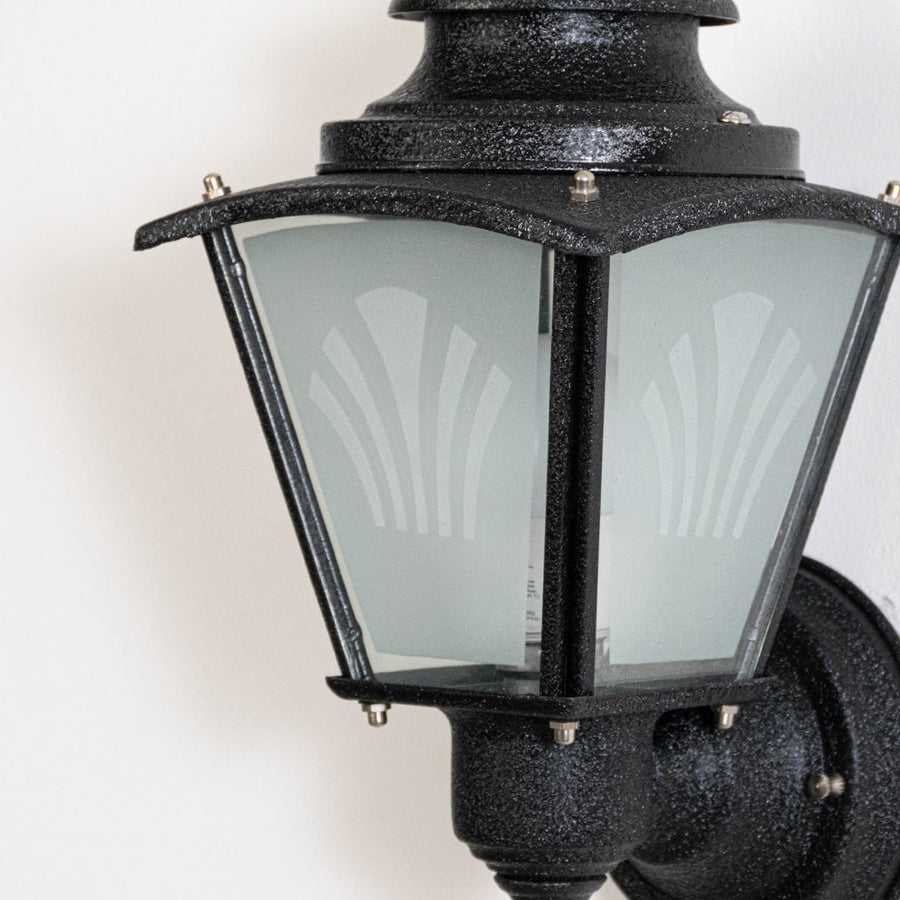 Closeup of black metal outdoor wall light highlighting textured finish frosted glass panels and traditional lantern styling.