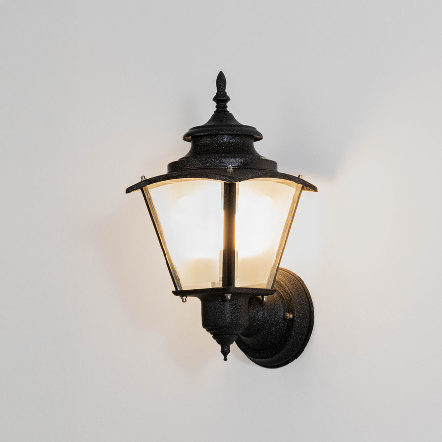 Black metal outdoor wall light on white background with clear glass shade for modern patio lighting decor.