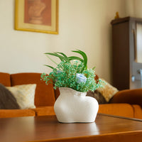 White textured ceramic vase with organic shape displayed on a wooden table  styled with green foliage and pastel flowers in a cozy living room setup.