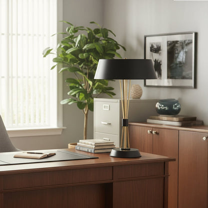 Black and gold metal table lamp with a sleek tapered base and wide shade placed on a wooden office desk creating warm ambient lighting in a modern workspace.