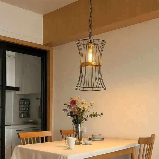 A hanging pendant light with a black wire cage shade and a warm glowing bulb, suspended above a dining table in a modern kitchen setting.