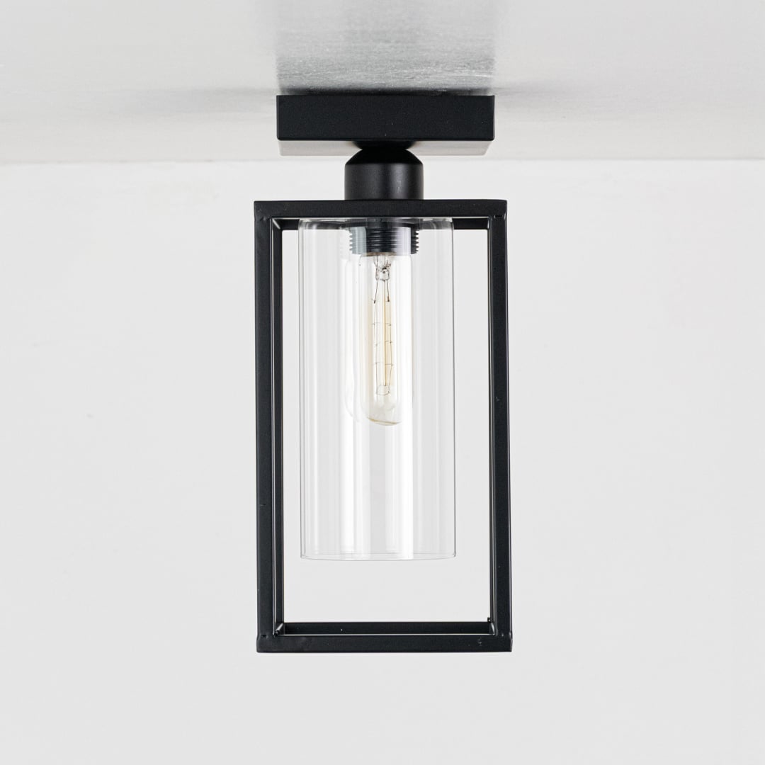 Black metal outdoor ceiling light with clear glass shade displayed with lights off on a clean white background showcasing its modern rectangular frame.