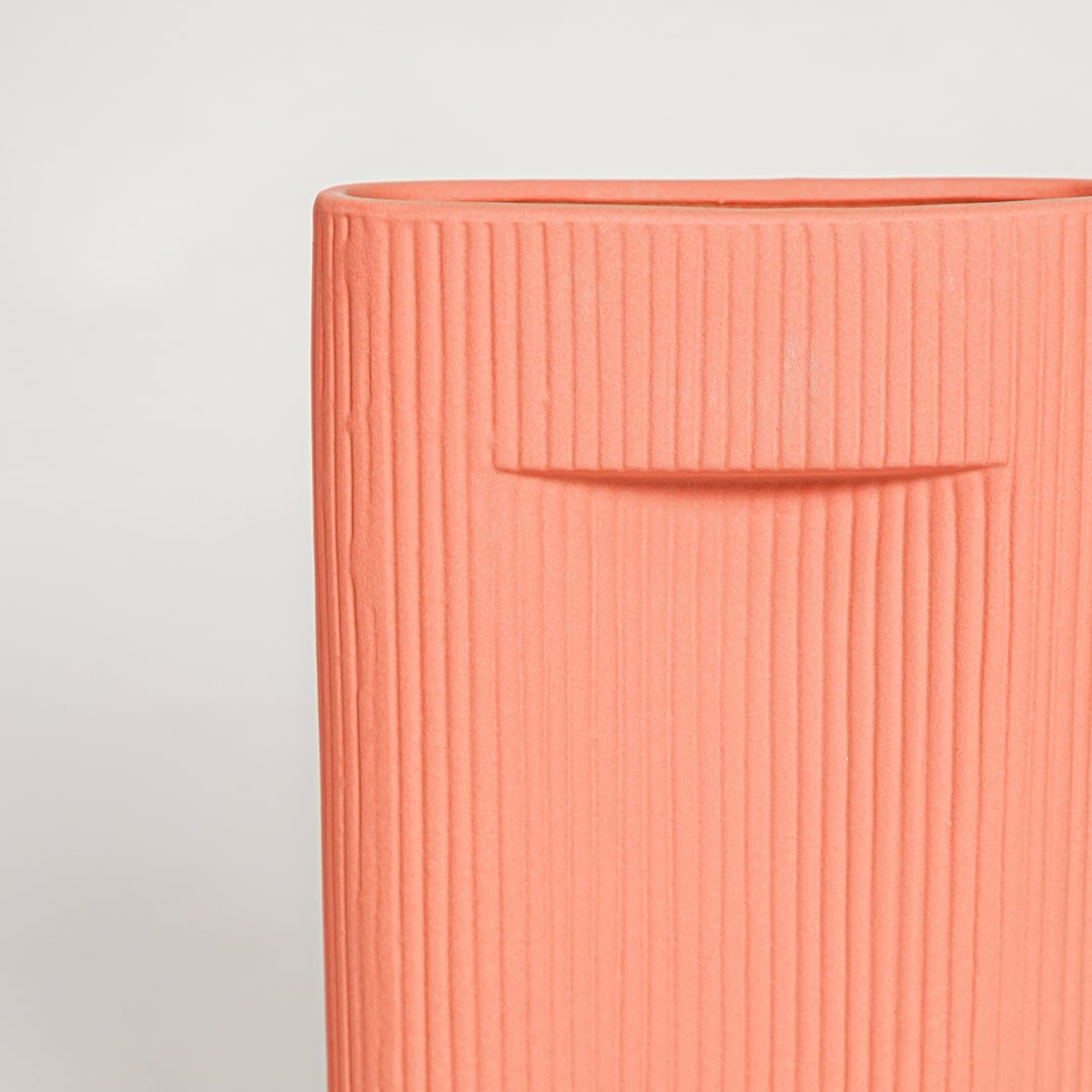 Closeup of matte coral ceramic vase with fine lined detailing ideal for elegant home decor shelf or side table styling.