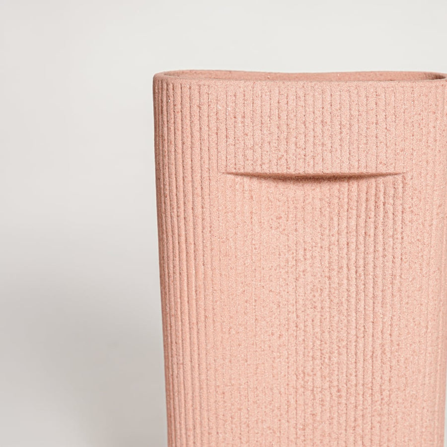 Closeup of matte peach ceramic vase with vertical lined texture ideal for elegant home decor shelf or side table styling.