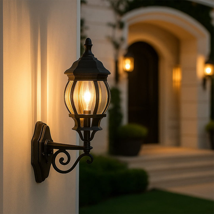 Illuminated black outdoor wall lantern with vertical ribbed glass mounted on white pillar near elegant arched home entrance.