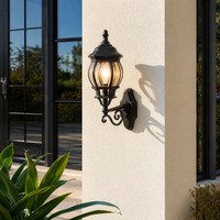 Ornate black iron curved scroll arm globe glass lantern wall sconce on stucco pillar for luxury estate courtyard patio.
