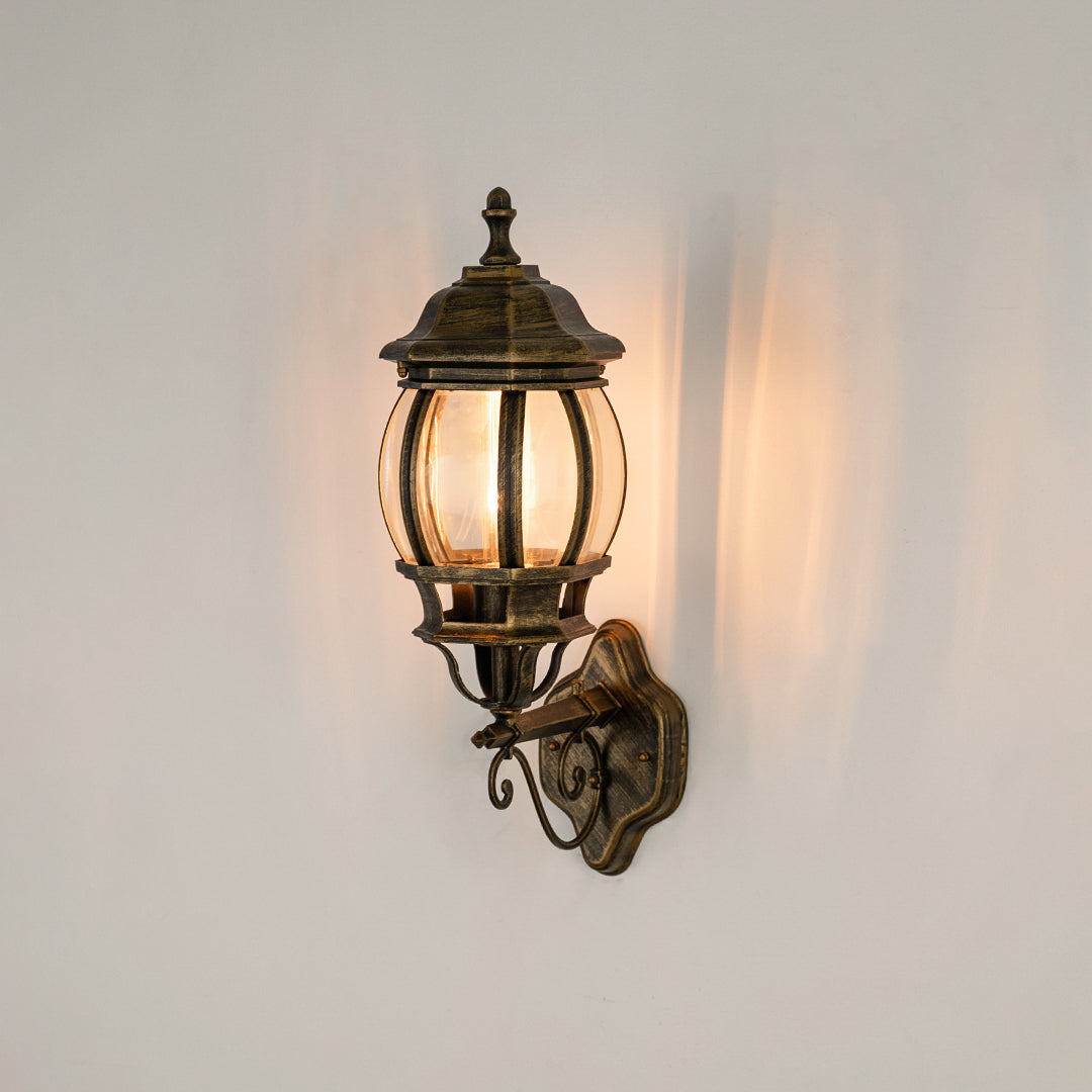 Antique brass outdoor wall sconce on white background with a rounded clear glass cage lantern for entry pathway decor.