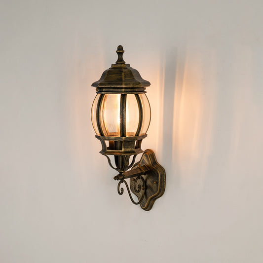 Antique brass outdoor wall sconce on white background with a rounded clear glass cage lantern for entry pathway decor.