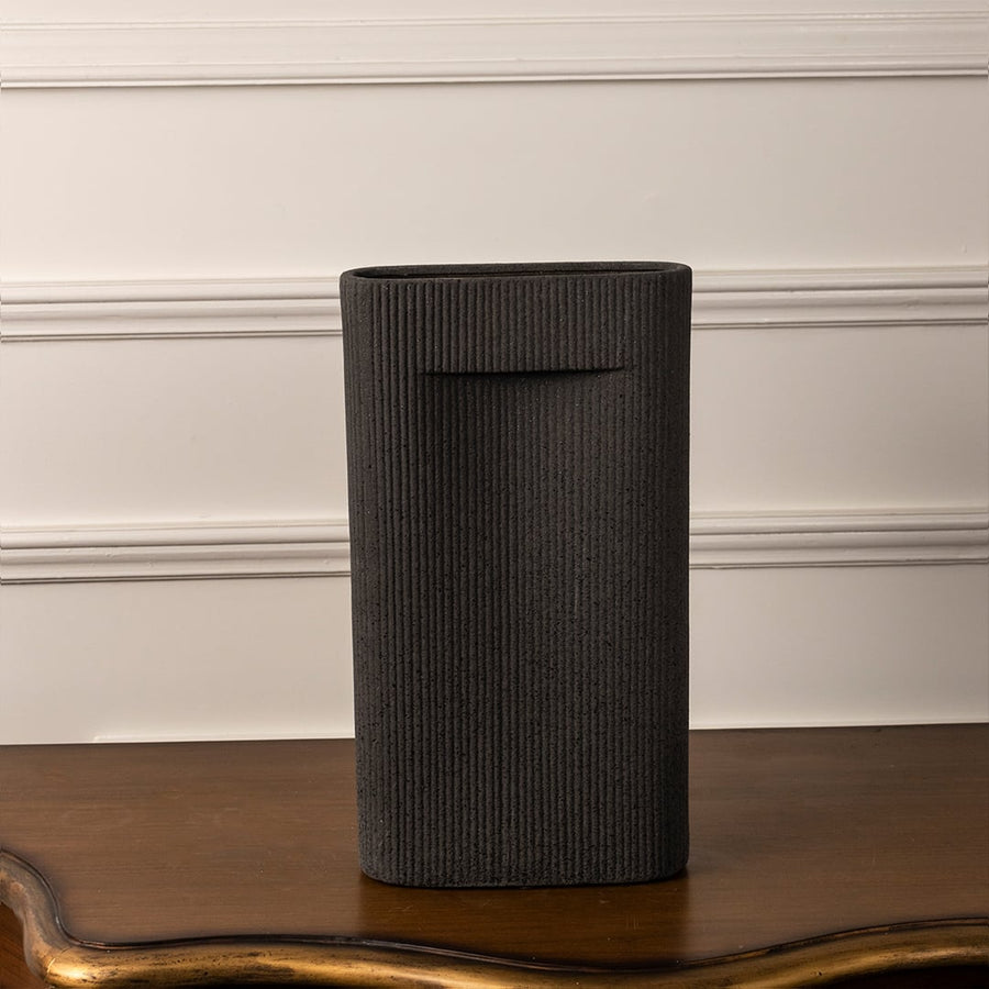 Matte black ribbed vase with sleek rectangular form standing on white background reflecting elegant modern artistry.