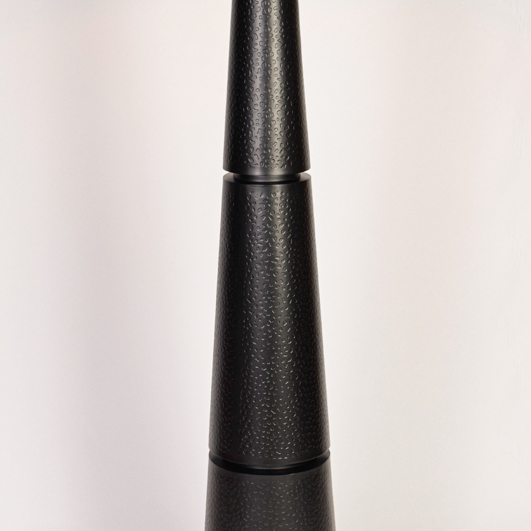 Closeup of black floor lamp base highlighting textured finish and stacked tapered form beneath clean white drum shade modern living spaces today.