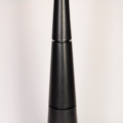 Closeup of black floor lamp base highlighting textured finish and stacked tapered form beneath clean white drum shade modern living spaces today.