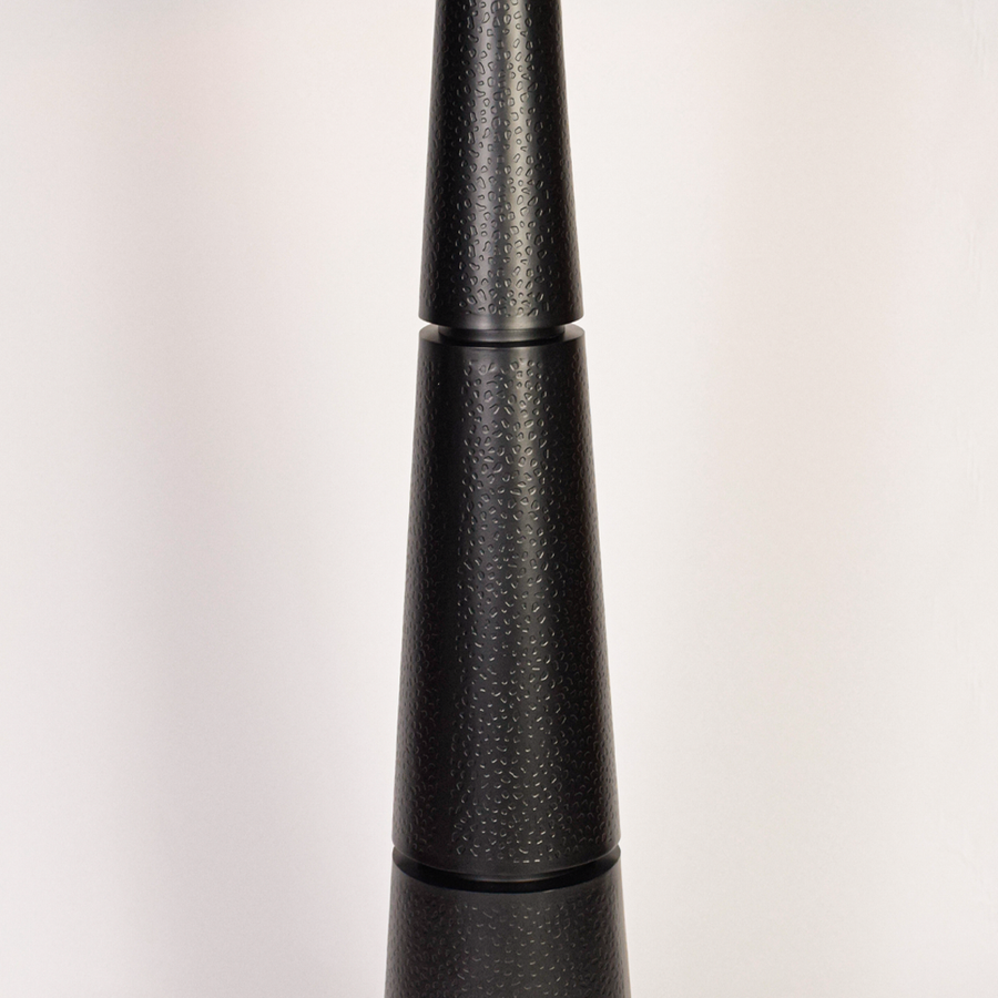 Closeup of black floor lamp base highlighting textured finish and stacked tapered form beneath clean white drum shade modern living spaces today.