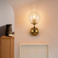 Modern gold metal wall light with clear glass globe for stylish bedroom and premium decor spaces.

