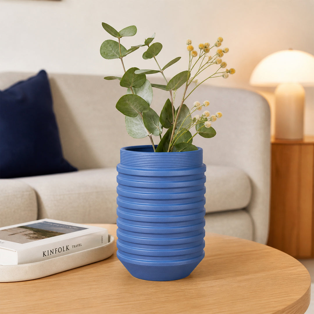 Blue textured ceramic flower vase with fresh stems placed on wooden table for stylish home decor styling.