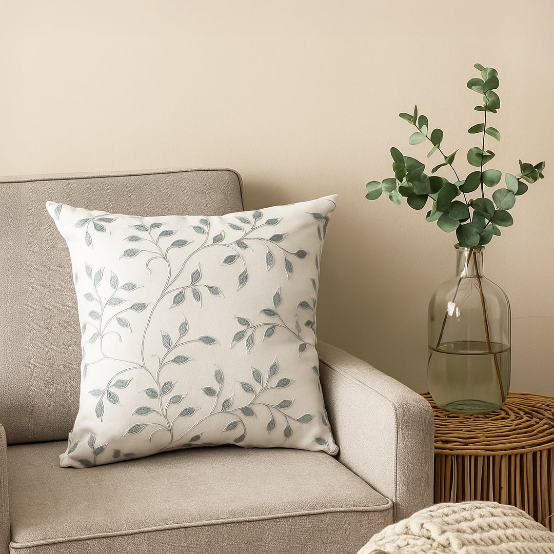 White cotton cushion cover with grey botanical embroidery displayed on a modern sofa adding an elegant nature inspired touch with a soft breathable and skin friendly fabric quality.