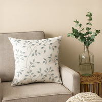 White cotton cushion cover with grey botanical embroidery displayed on a modern sofa adding an elegant nature inspired touch with a soft breathable and skin friendly fabric quality.