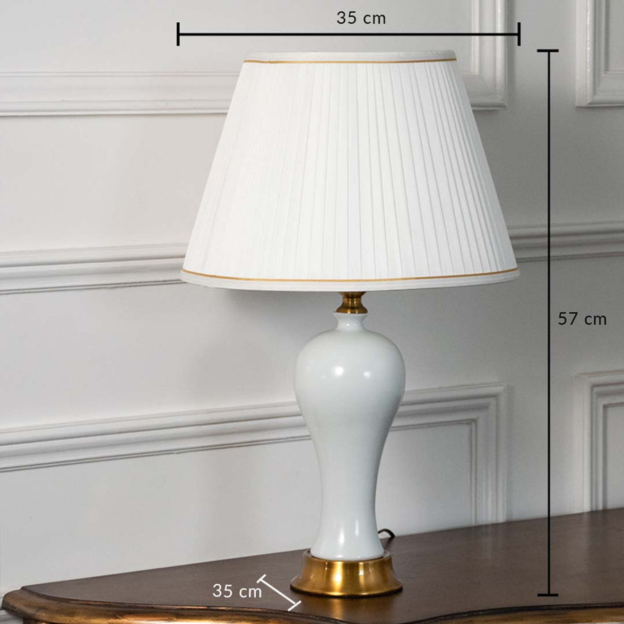 White ceramic table lamp with gold base and pleated shade shown with clear dimensions of 35 cm width and 57 cm height ideal for bedside or console placement.