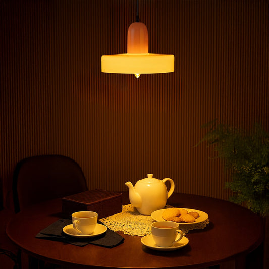 Pink and olive green pendant ceiling light glowing warmly above dining table with tea set creating cozy lifestyle atmosphere.