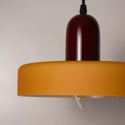 Closeup view of a modern pendant light showing the smooth colored shade and bulb detail with light on against a black background highlighting material and finish.