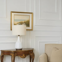 White ceramic table lamp placed on a wooden console table near an armchair adding a warm and sophisticated glow to the living room decor.