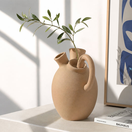 Beige ceramic flower vase with green stems placed on table for stylish contemporary home decor styling.