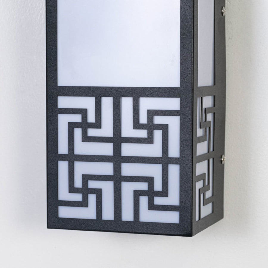 Closeup of black outdoor wall light featuring geometric cut metal frame frosted diffuser and modern architectural detailing.