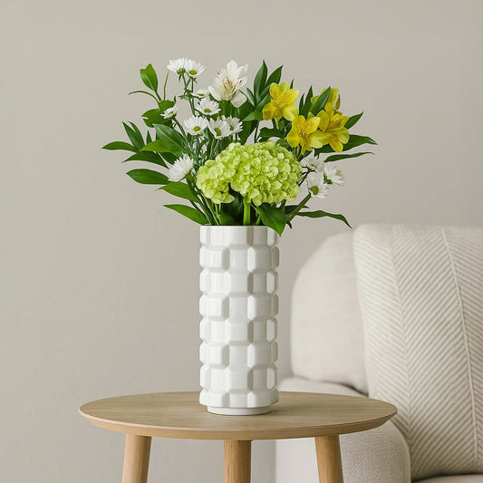White ceramic flower vase with green foliage placed on round wooden table near sofa creating fresh and elegant home decor style.