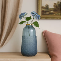 Blue ceramic vase with floral stems styled beside sofa and cushion creating balanced serene mood for interior Decor.