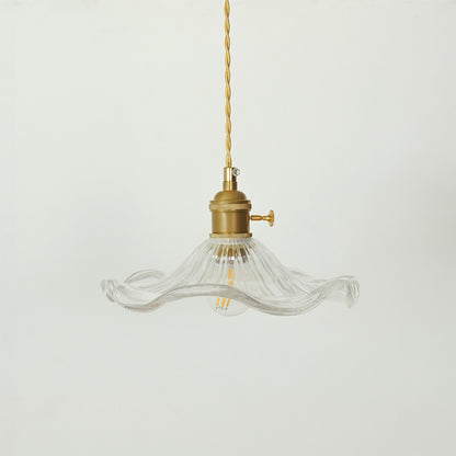 A vintage-style pendant light with a clear ribbed glass shade that has a wavy, flared rim and a brass-colored metal fixture and cord, shown against a plain light gray background.