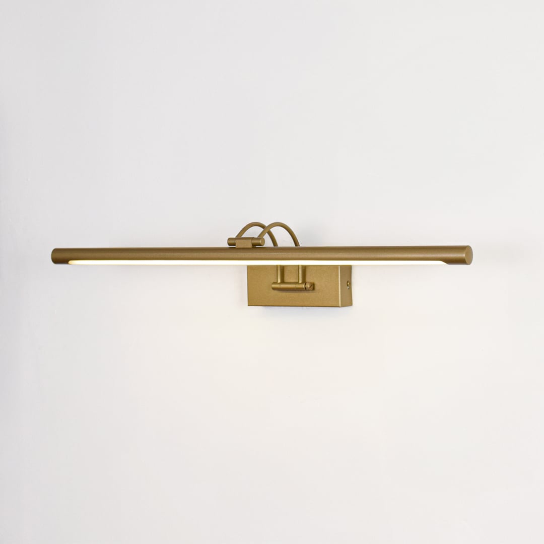 Gold metal picture light switched on over white background spreading soft warm glow ideal for gallery wall lighting.