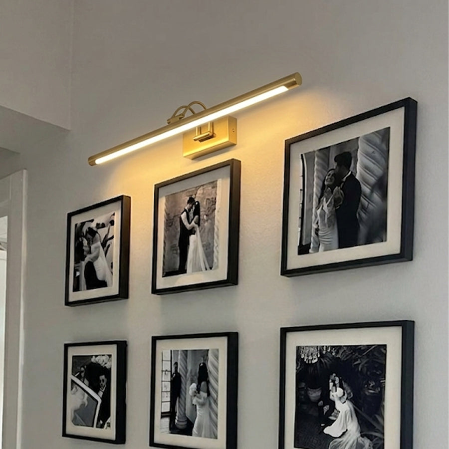 Gold metal picture light casting warm illumination above framed artwork creating elegant gallery style wall decor.
