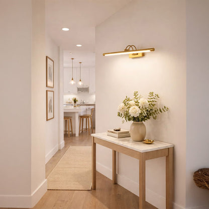 Gold metal picture light enhancing hallway artwork with warm illumination creating sophisticated interior ambiance.