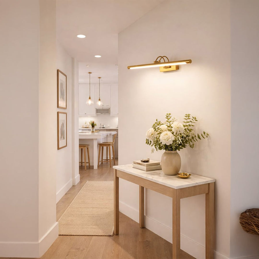 Gold metal picture light enhancing hallway artwork with warm illumination creating sophisticated interior ambiance.
