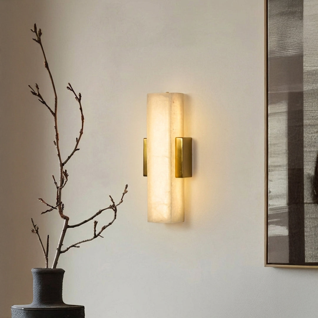 Modern wall light with vertical frosted glass shade mounted on textured wall beside decor branch ideal for ambient interior lighting.