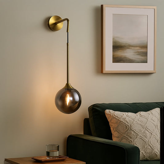 Smoked glass globe wall light with elegant brass arm turned off on white wall showcasing minimal and modern lighting style.