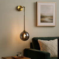 Smoked glass globe wall light with elegant brass arm turned off on white wall showcasing minimal and modern lighting style.