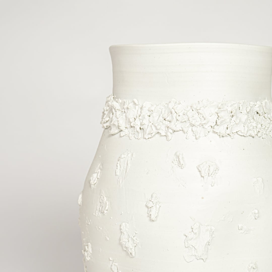 Closeup of white glazed ceramic vase with intricate raised detailing ideal for elegant home decor shelf or side table styling.
