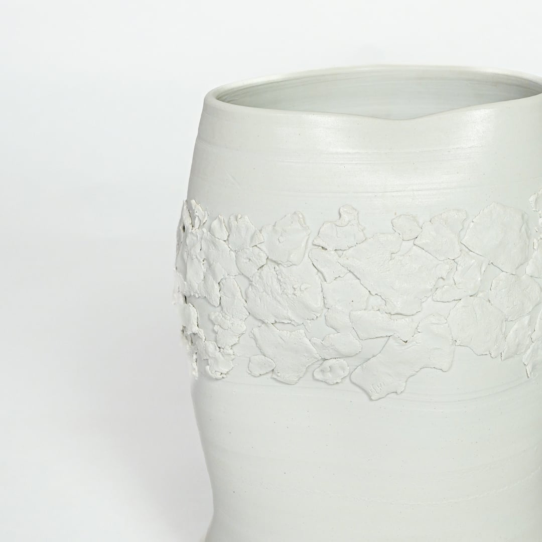 Detailed closeup of white ceramic vase showcasing embossed floral band and refined matte finish.