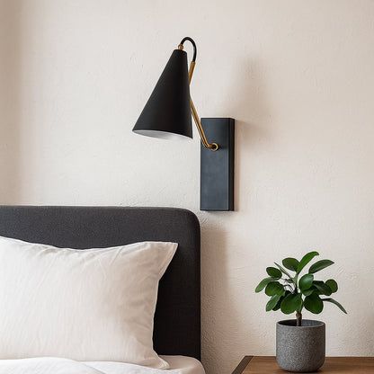 Black wall light with conical shade and gold arm mounted above bedside table with plant styled in modern bedroom interior.