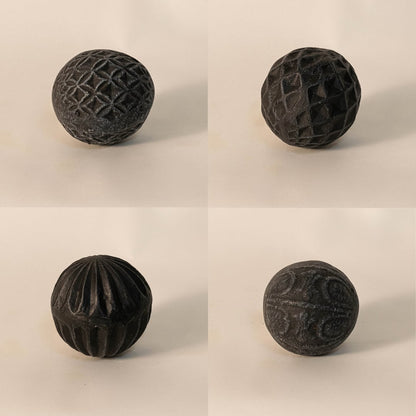Close-up of black carved ball emphasizing intricate handcrafted pattern and rough matte ceramic texture.