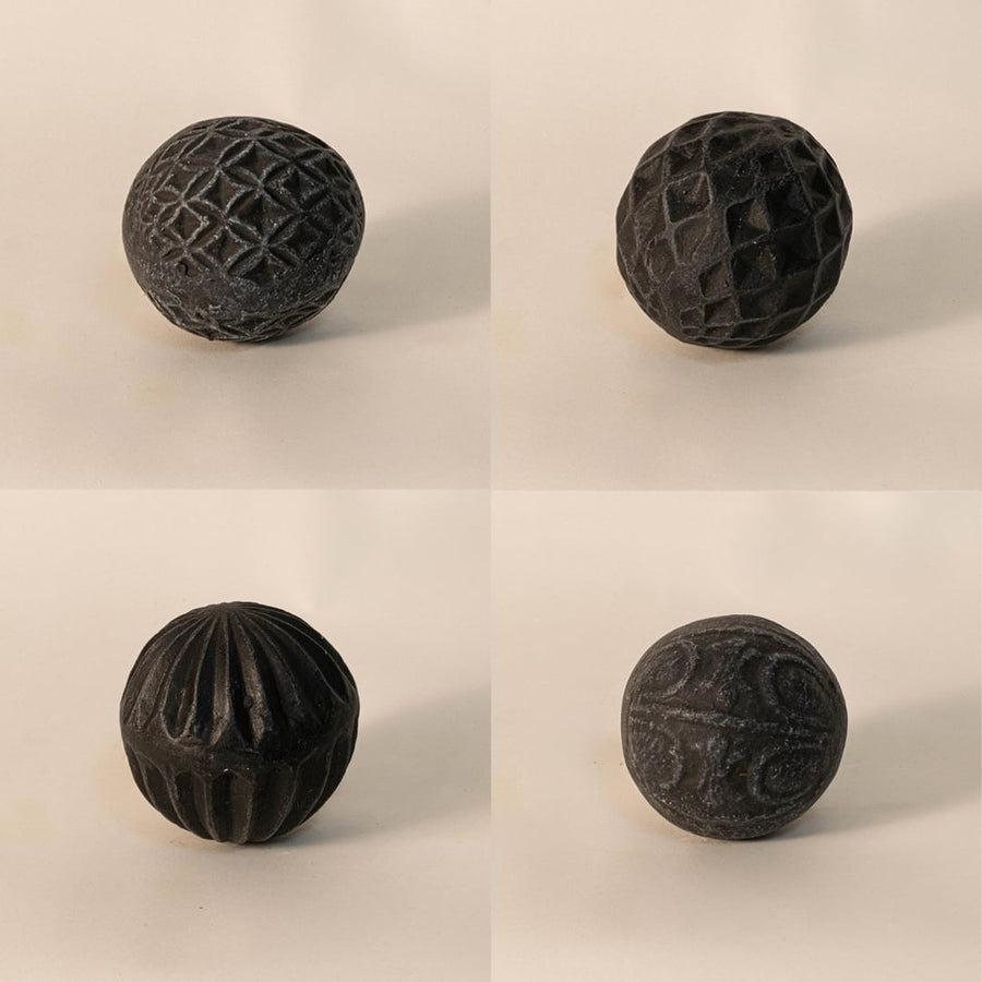 Close-up of black carved ball emphasizing intricate handcrafted pattern and rough matte ceramic texture.